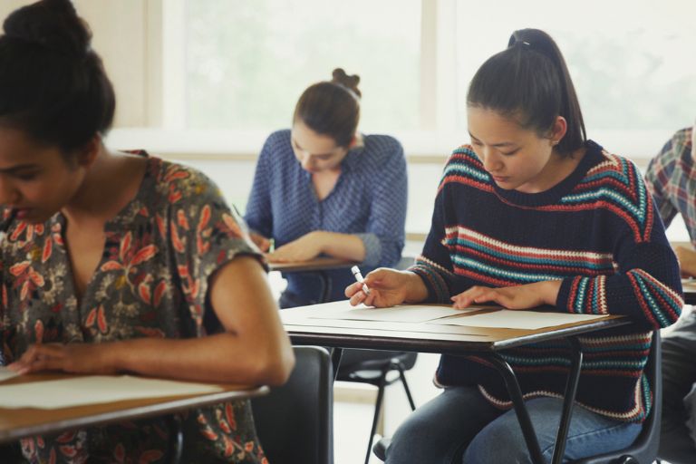 International doctors sitting at desks focused on writing essays for the IELTS academic UKVI writing task in a classroom setting.